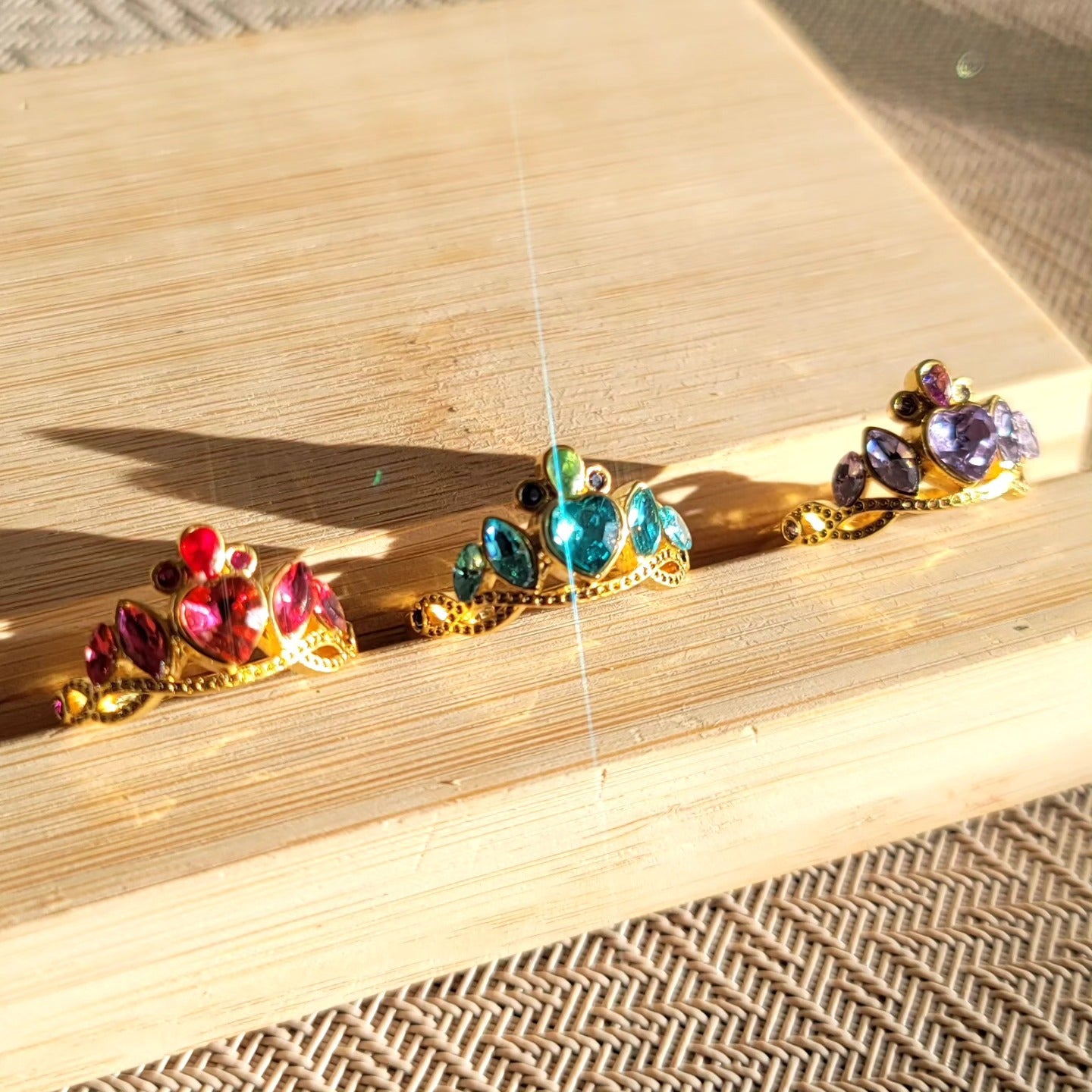Anillos de princesas Disney, cada uno con un dije en forma de corona en diferentes colores: fucsia, blanco y morado.