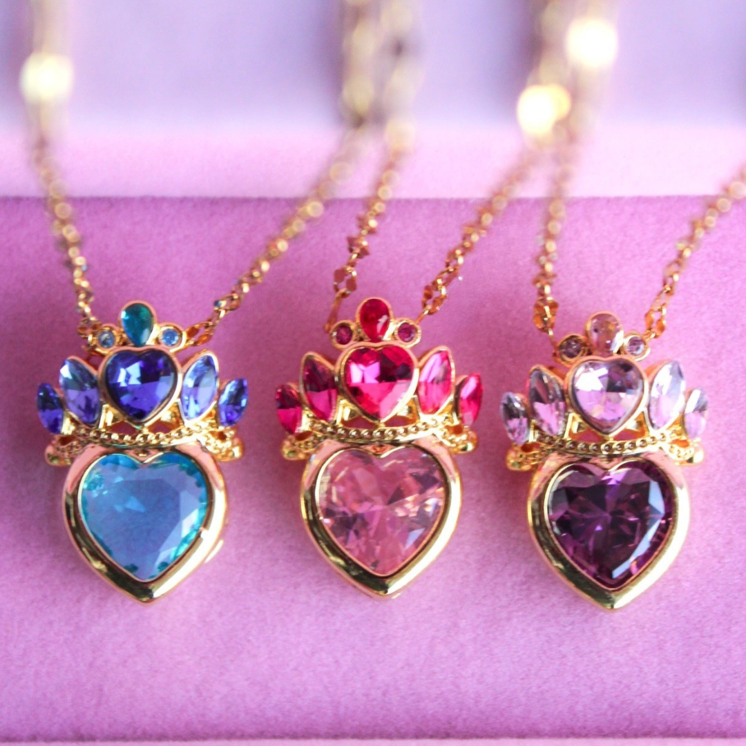 Tres collares de princesas Disney, cada uno con un dije de corazón y corona en diferentes colores: azul, fucsia y morado.