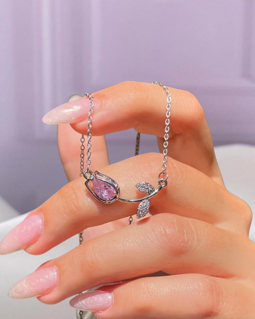 Collar de tulipán con dije de cristal rosa y cadena plateada, sostenido por una mano.
a
