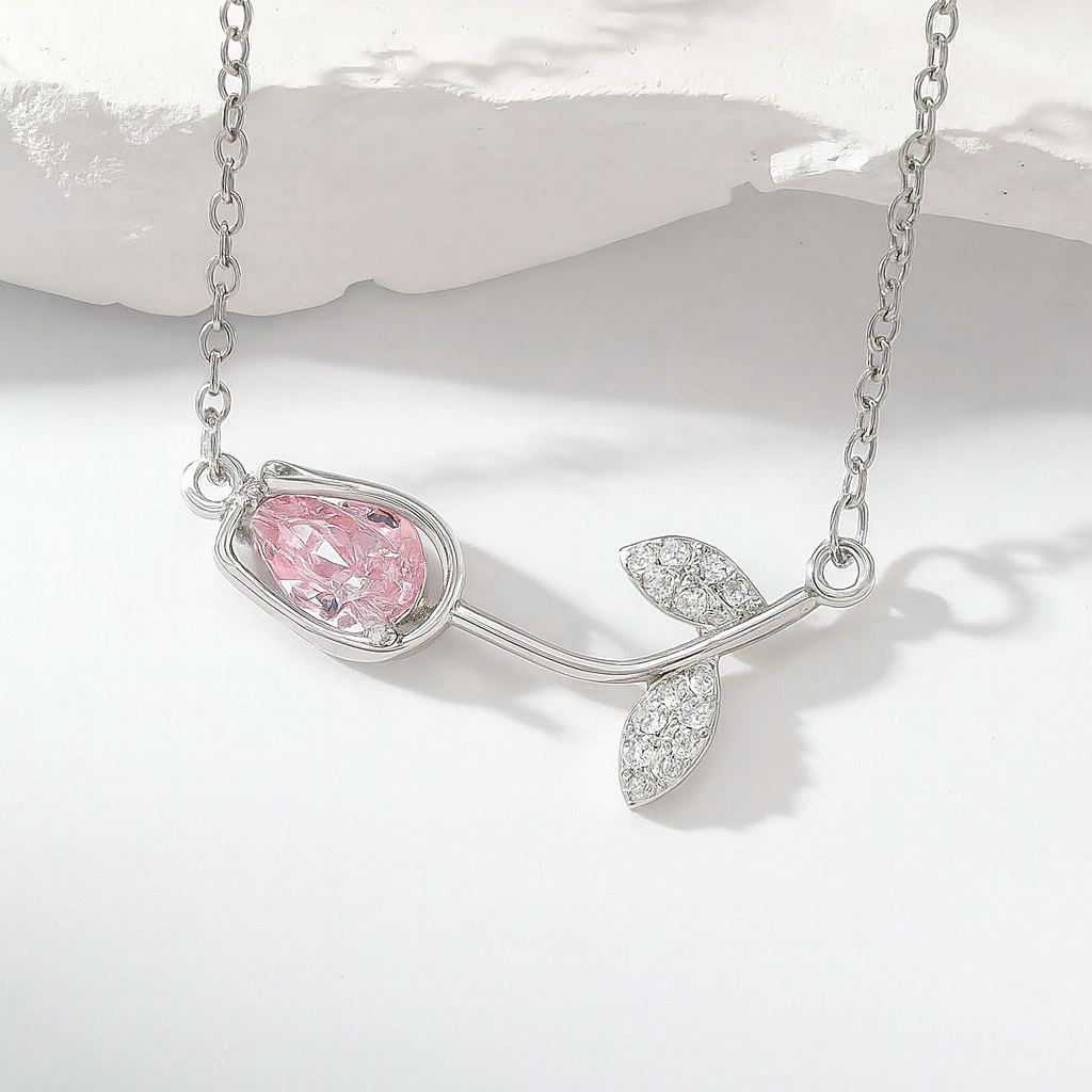 Collar de tulipán con dije de cristal rosa y cadena plateada, sostenido por una mano.
