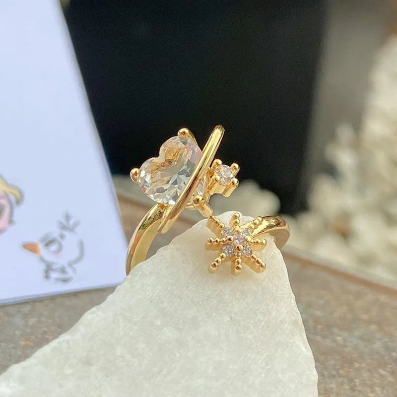 Anillo ajustable del Corazón Cósmico en acabado dorado con piedras en forma de corazón y estrellas. blanco