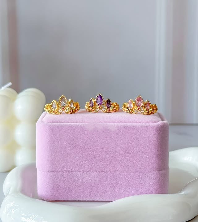 Anillo de corona de princesa Rapunzel con circones de colores fucsia, lila y blanco sobre una caja