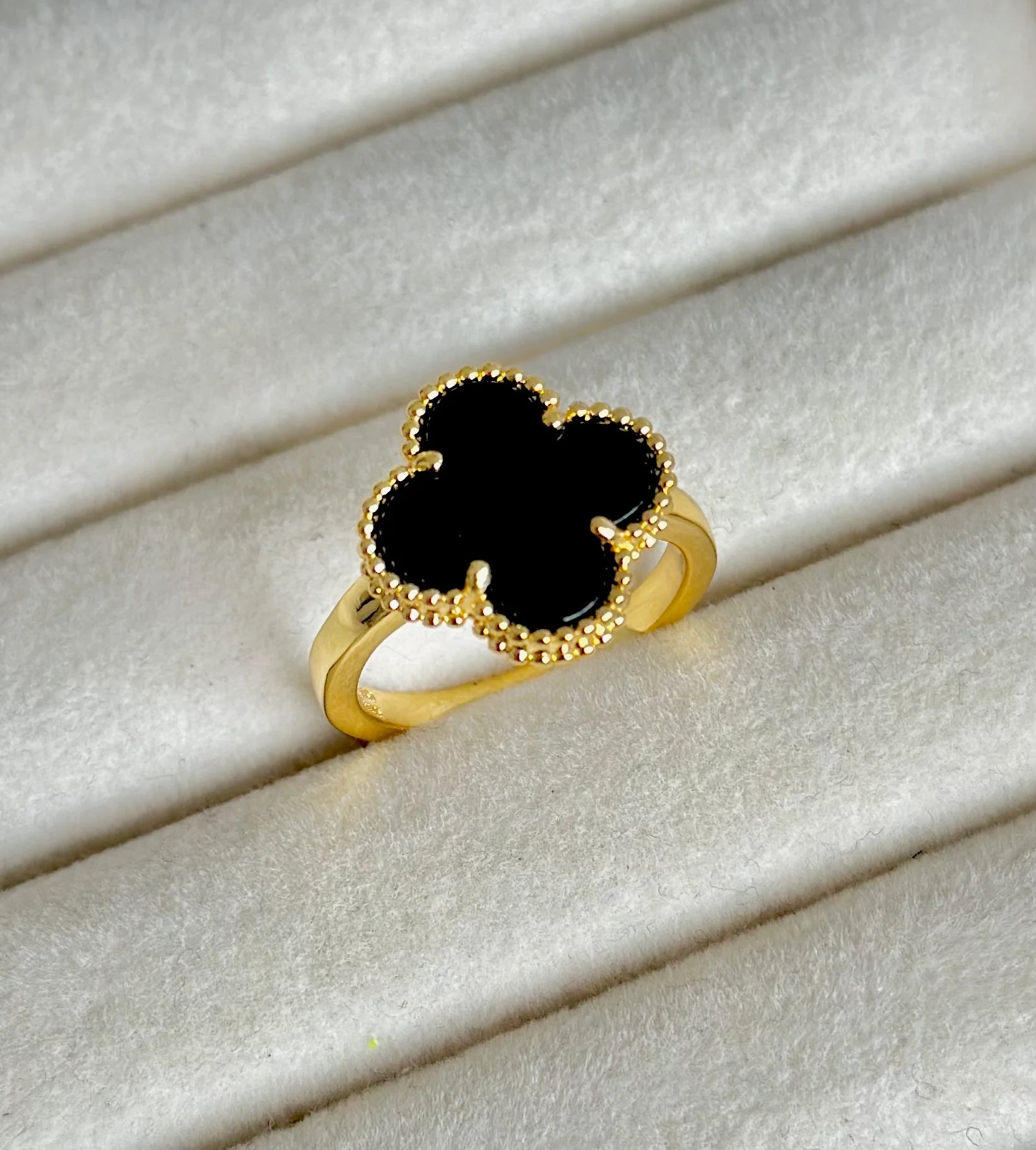 Anillo de acero inoxidable en tono dorado con un dije de trébol negro, inspirado en Van Cleef.