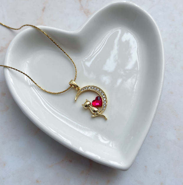 Collar con dije de gatito sentado en una luna, con un corazón central de cristal rojo y acabado dorado.