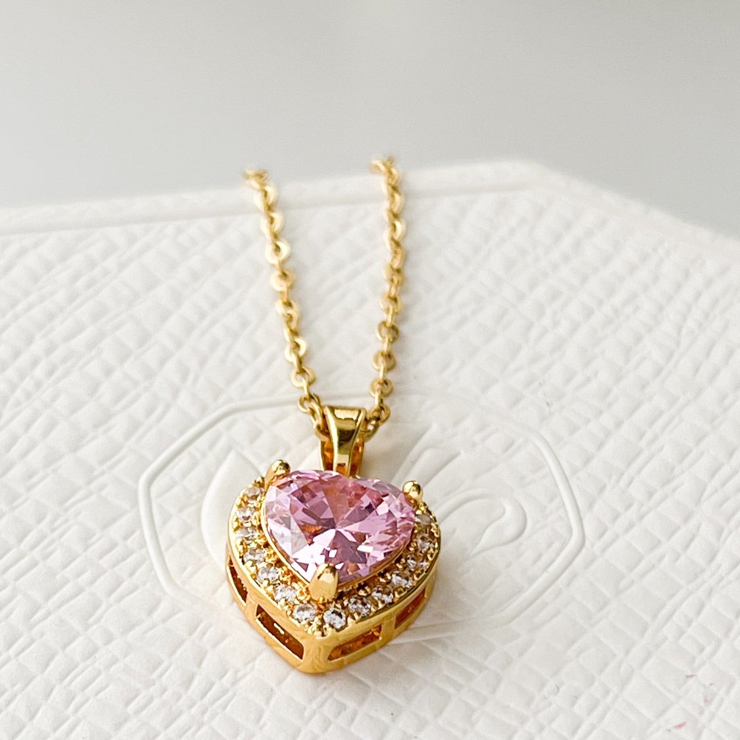 Collar con dije de corazón en color dorado, con una piedra central rosada y borde de circonias.