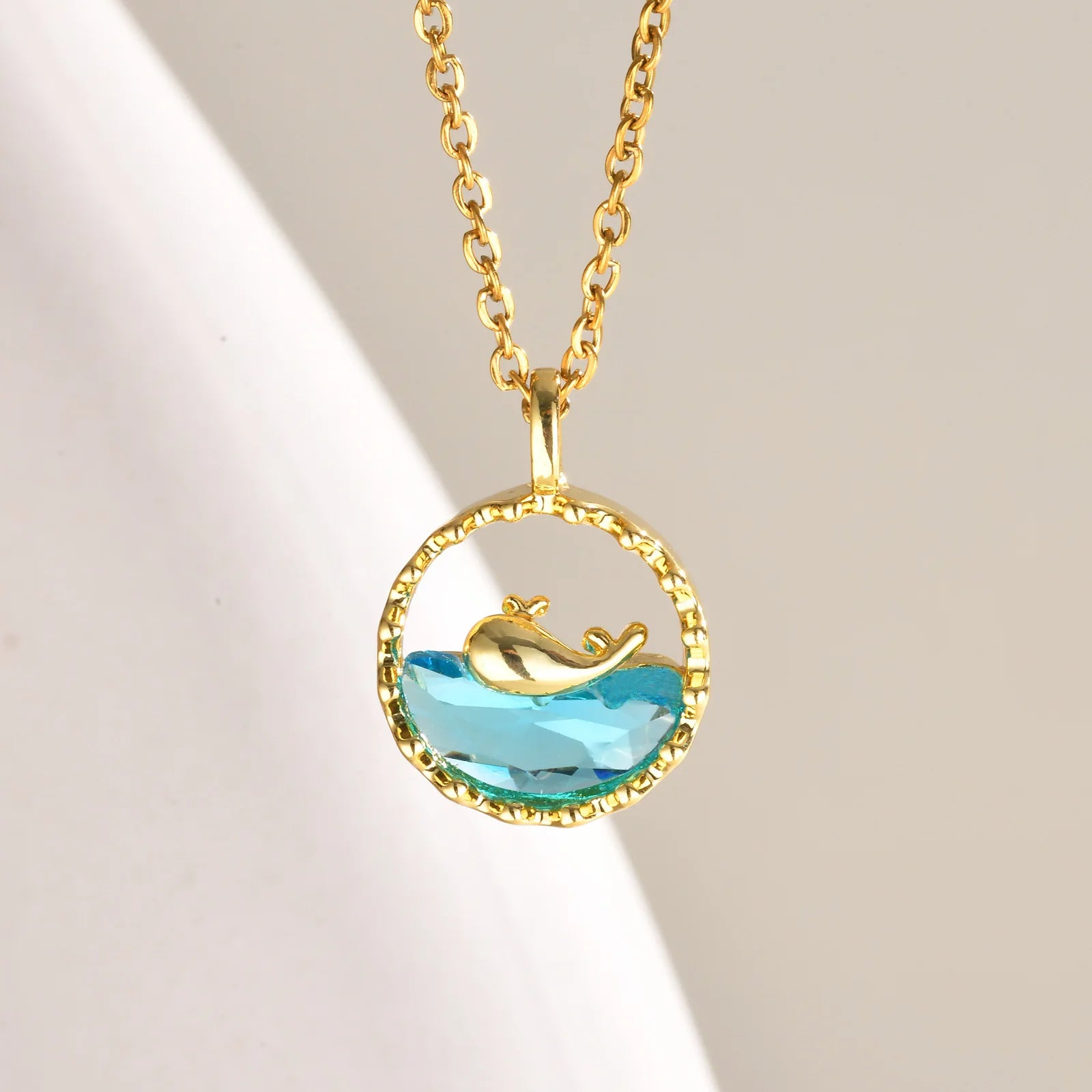 Collar de ballena en un círculo dorado, con una base de vidrio azul.
