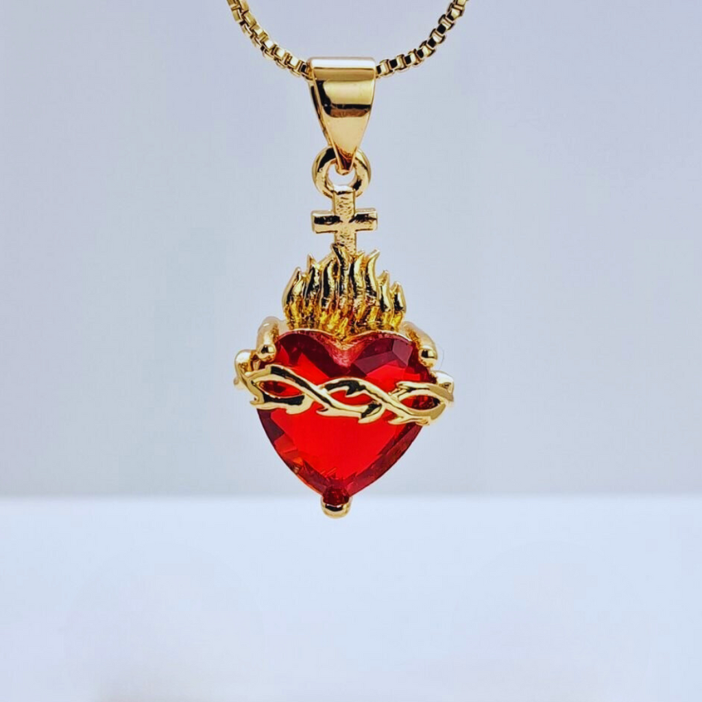 Collar con dije del Sagrado Corazón en color dorado, con un corazón central de cristal rojo, una corona de espinas, llamas y una cruz.

