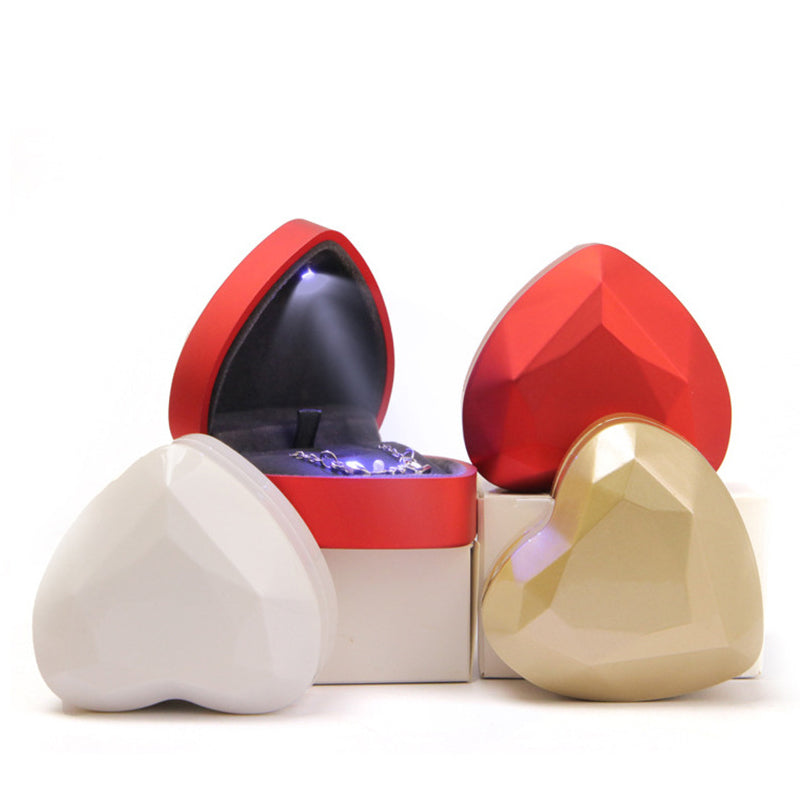 Varias cajas de joyería rojas dorada, blanca y azul con forma de corazón y un modelo abierto mostrando la luz interna.