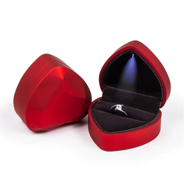 Caja de regalo roja con forma de corazón facetado, con una luz LED interna que ilumina un anillo.