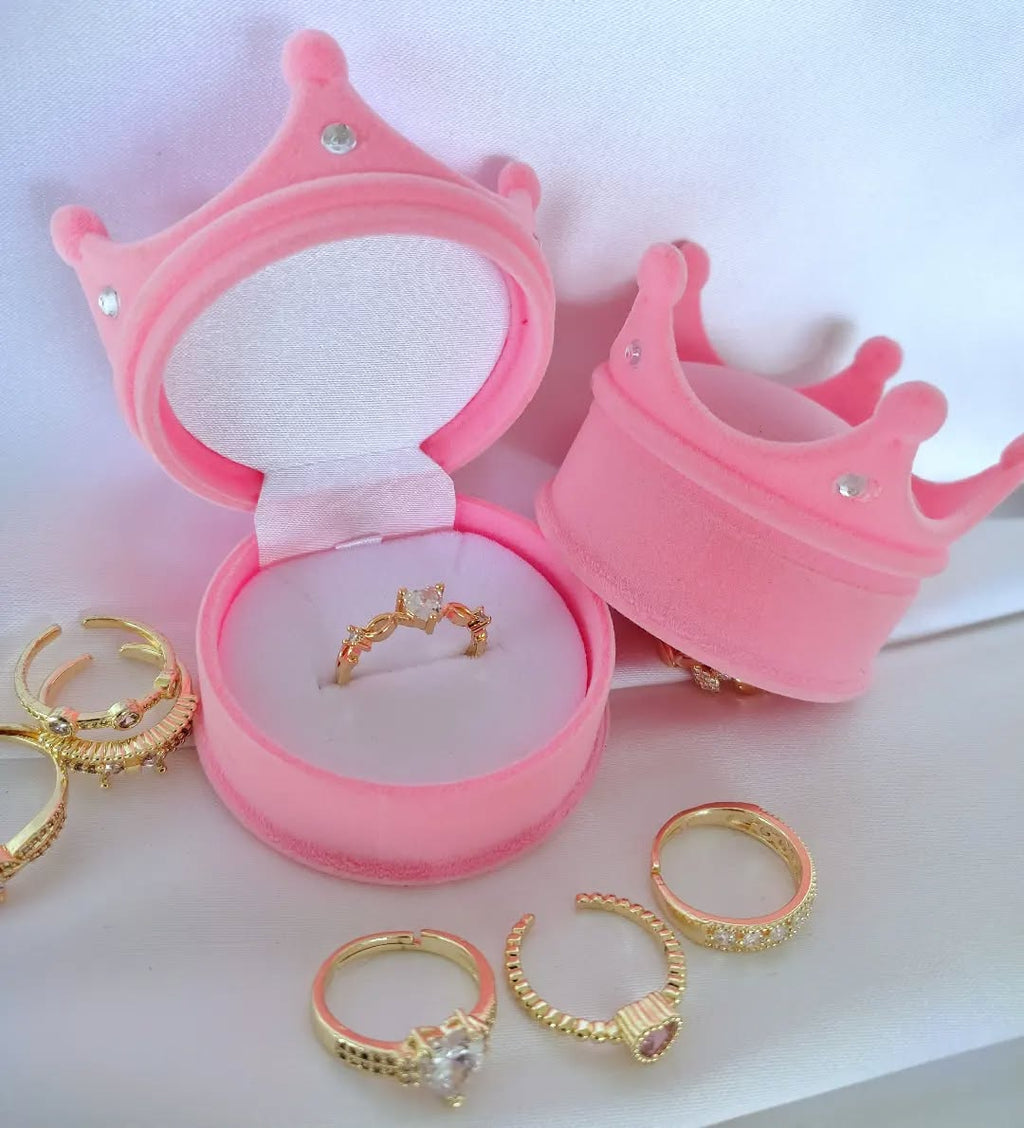 Caja de joyería rosa en forma de corona, abierta, mostrando el interior acolchado para un anillo.
