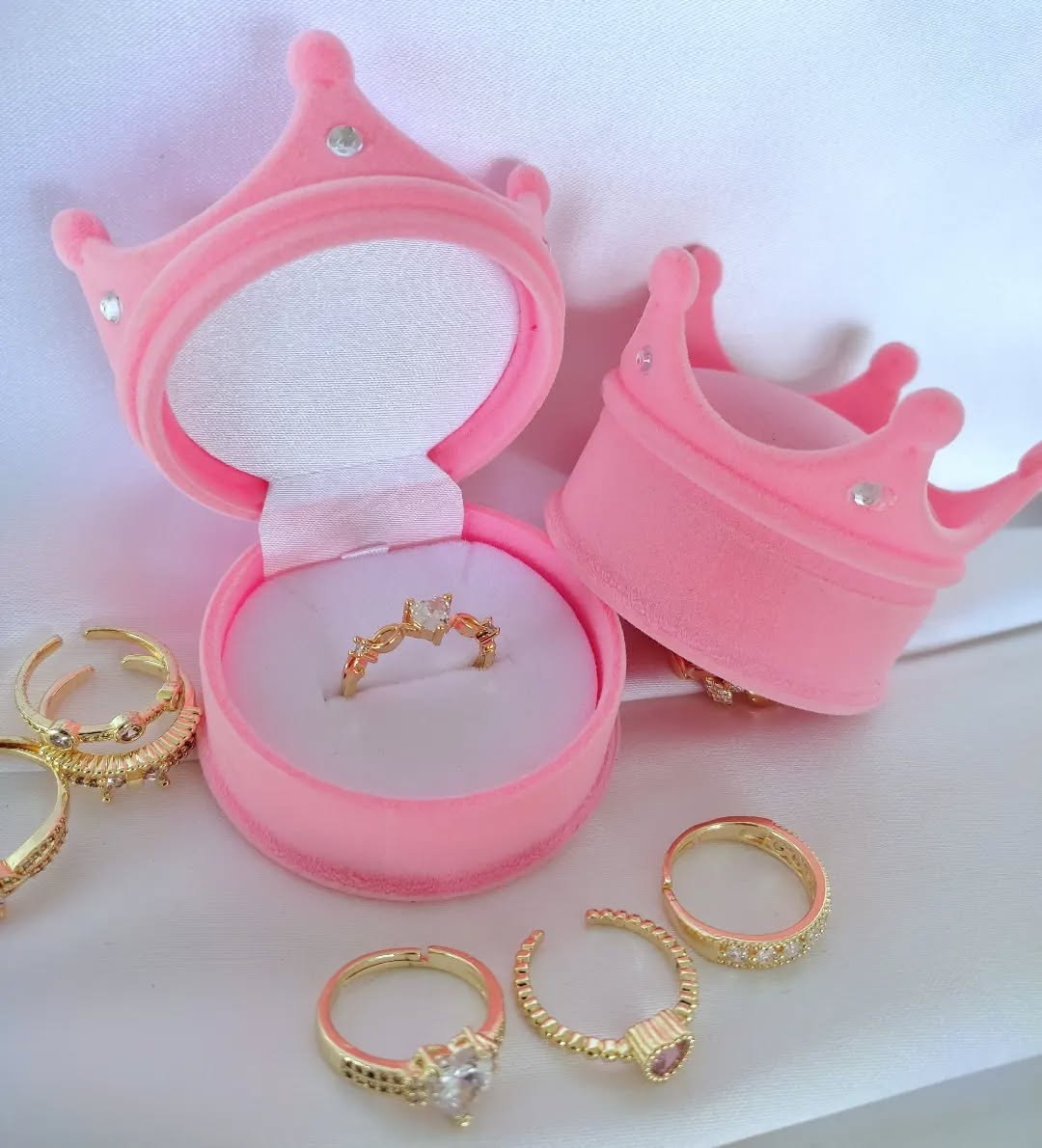 Caja de joyería rosa en forma de corona, abierta, mostrando el interior acolchado para un anillo.