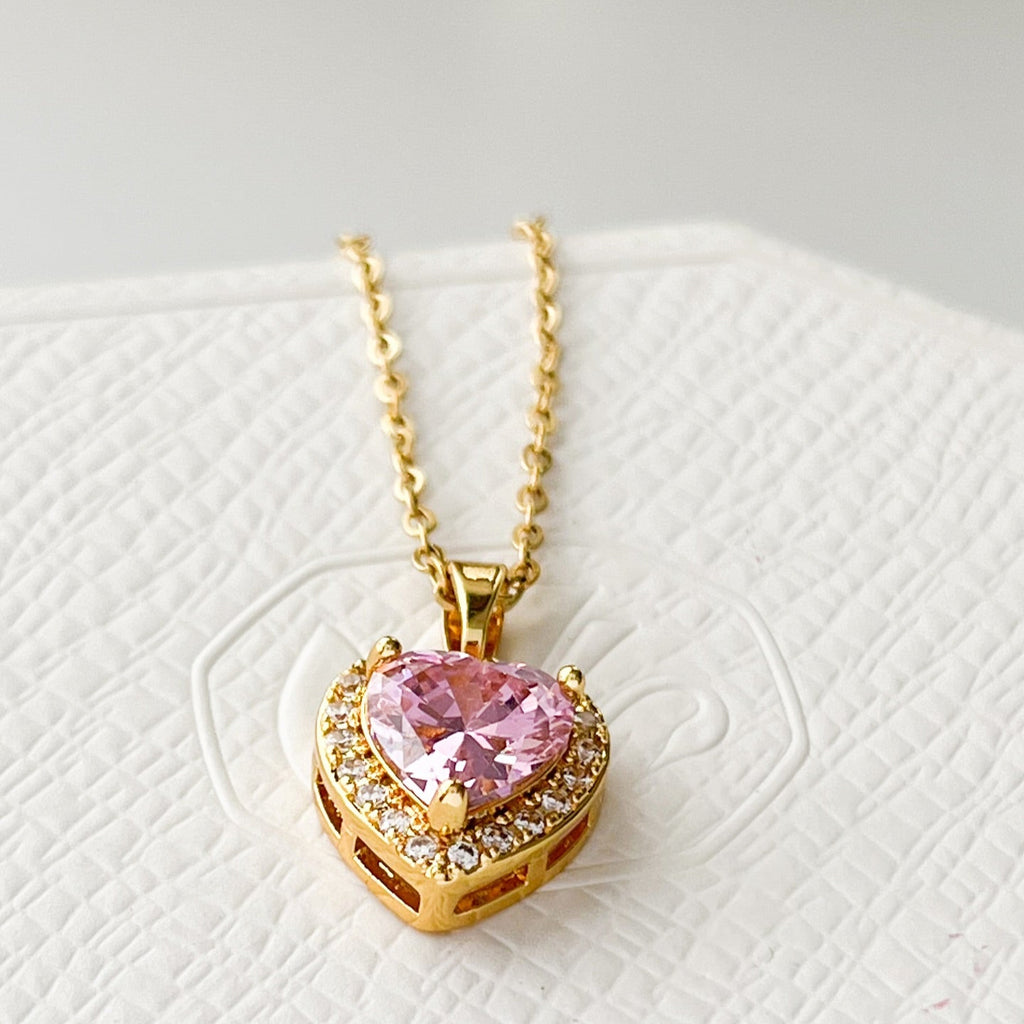 Collar con dije de corazón en color dorado, con una piedra central rosada y borde de circonias.
