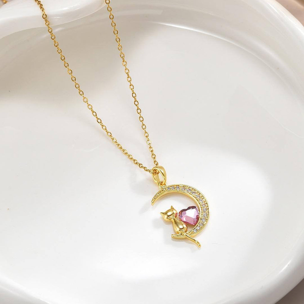 Collar con dije de gatito sentado en una luna, con un corazón central de cristal rosa y acabado dorado.
